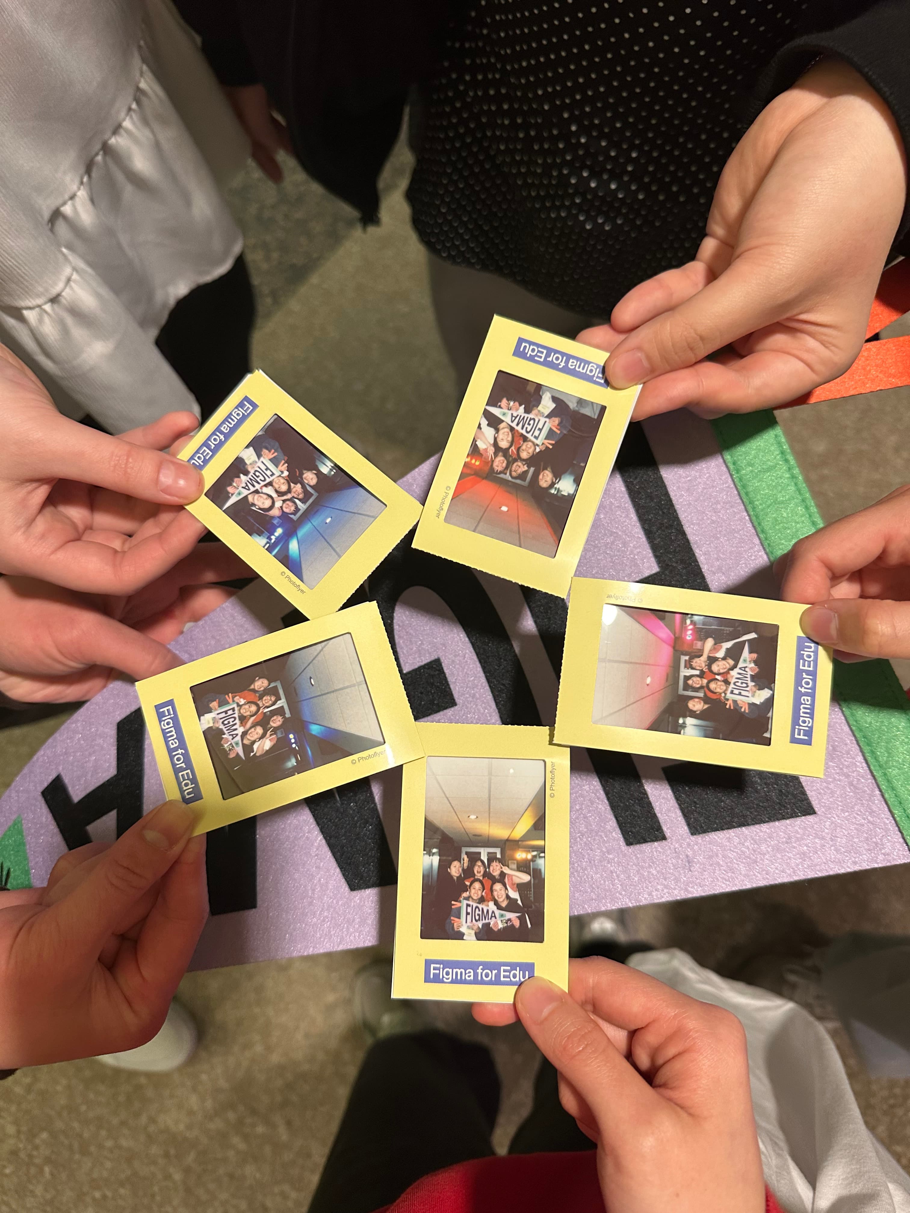 Five pairs of hands holding Figma for Edu instant photos in a circle.